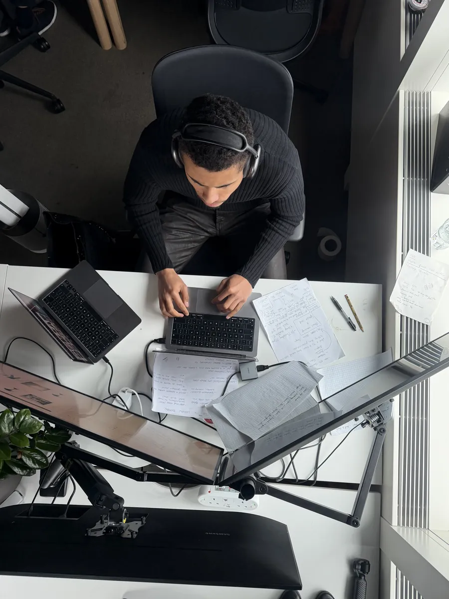 Overhead view of a team member at a desk with laptops and headphones