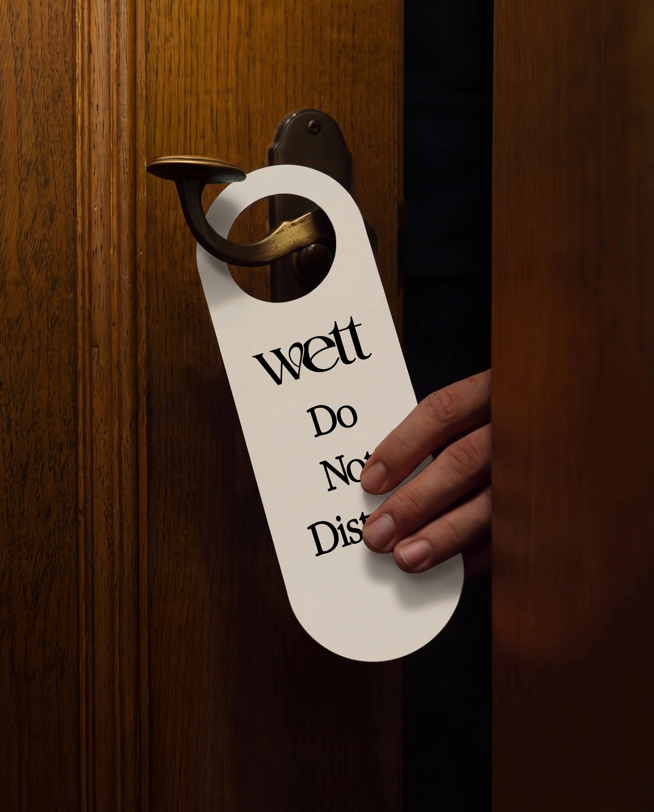 A hand hanging a Wett ‘Do not disturb’ sign on a hotel door.