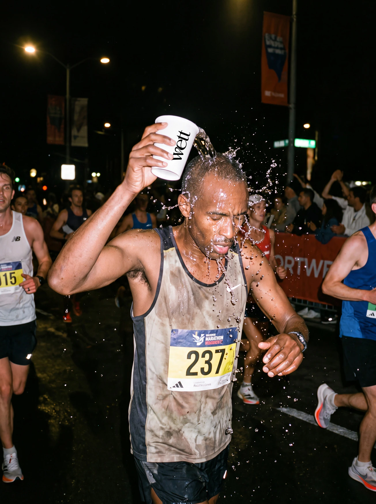 A marathon runner splashing water from a Wett cup over himself at night.