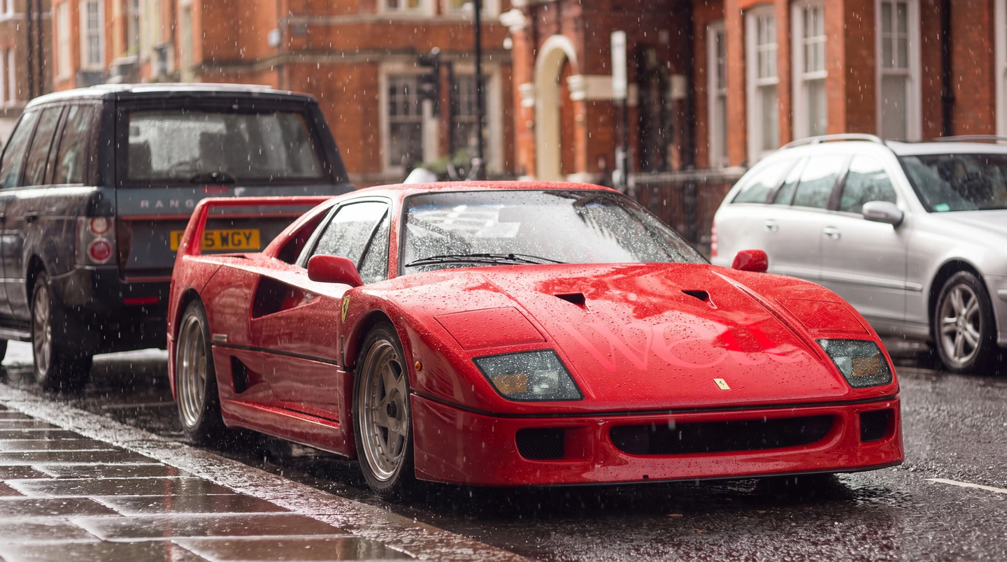 A red Ferrari parked on a rainy London street, the Wett logo showing dry on its bonnet.