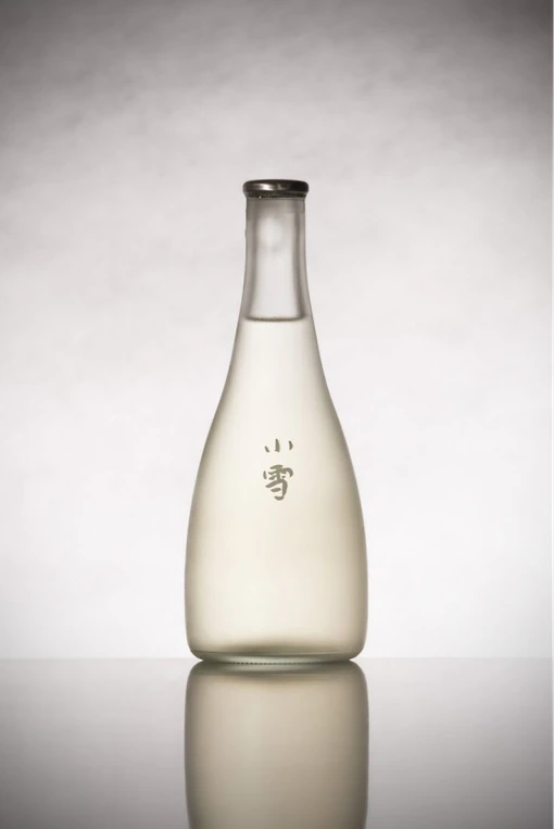 A slim frosted sake bottle on a grey background.