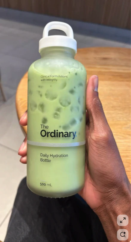 A hand holding a frosted bottle of green drink.