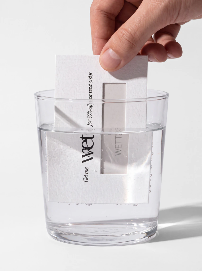 A hand dipping the Wett card into a glass of water.