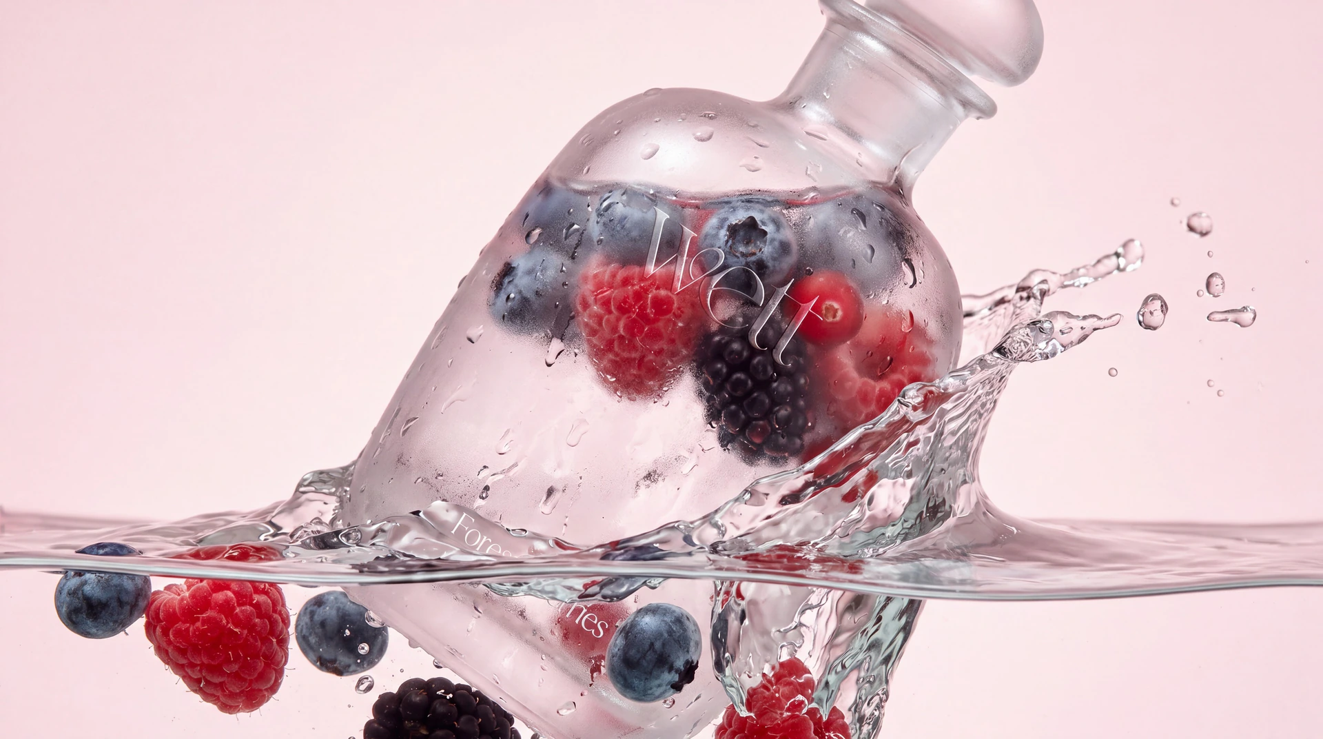 The frosted Wett bottle filled with raspberries, blueberries and blackberries, splashing into water on a pale pink background.